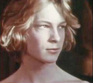 Caucasian male with tousled blond hair to the jawline, head turned to the left.